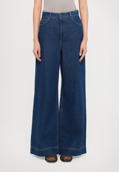 Weite Jeans aus dunkelblauem Denim, mit hoher Taille, Knopfverschluss und Fronttaschen. Der Stoff hat eine glatte Textur.