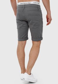 Grå denimshorts med opfoldet kant og en hvid talje, der har "Calvin Klein"-logoet. Baglommerne har et subtilt skråt design.