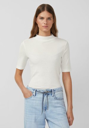 Weißes Kurzarm-Mock-Neck-Top, gerippte Textur, figurnahe Passform, kombiniert mit hellblauen Jeanshosen mit Kordelzugbund.