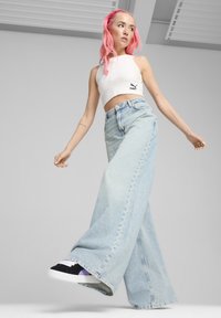 Lichtblauwe wijde jeans, met hoge taille en een onafgewerkt zoom. Gecombineerd met een witte crop top en zwarte sneakers, wat een casual look creëert.