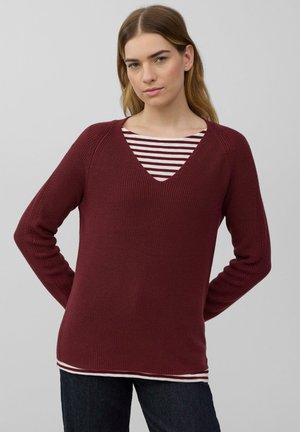 Pull en tricot bordeaux avec un décolleté en V profond, présentant une superposition rayée en dessous et une texture côtelée aux poignets et à l'ourlet.