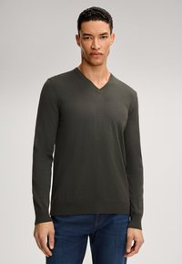Maglione verde scuro a scollo a V realizzato in tessuto knit leggero, con maniche lunghe e polsini a coste, abbinato a jeans in denim blu.