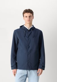 Navy blue waterproof jacket with a hood, front snap closures, adjustable hem, and Velcro cuffs. Smooth fabric texture, relaxed fit.