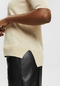 Beige strikket sweater med korte ærmer og skrå kant, parret med en sort læderskirt, der viser glatte teksturer og kontrasterende farver.