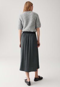 Pullover grigio fluffy a maniche corte abbinato a una lunga gonna verde scuro fluida. Un paio di semplici scarpe nere completano l'outfit.