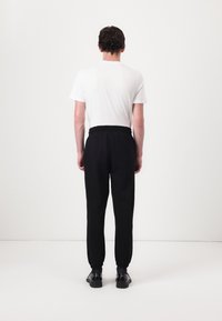 Black sweatpants with an elastic waist and cuffs, paired with a plain white T-shirt, viewed from the back. Smooth fabric, minimal design.