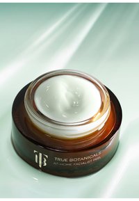 Amberkleurig glazen potje met een witte crème erin. Etiket met de tekst "True Botanicals At-Home Facialist Peel." Gladde, ronde deksel; glanzende afwerking.