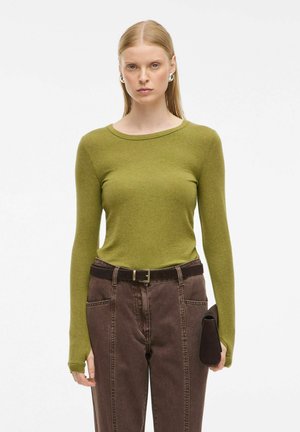 Olivno zelena dolga majica s krojem okroglega izreza, v kombinaciji z temno rjavimi hlačami z visokim pasom. Obleka vključuje črn pas in torbico.