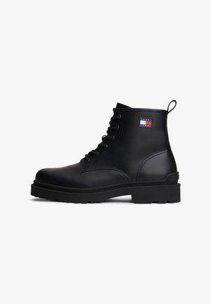 Bota de tobillo negra de cuero con cordones, lengüeta para tirar y parche con el logo de Tommy Jeans en el costado, suela resistente para uso en exteriores.