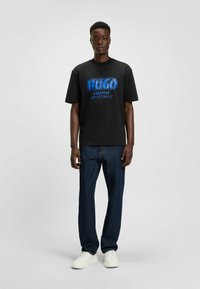 Czarna bawełniana koszulka z niebieskim graficznym napisem "HUGO CREATIVE DEPARTMENT", w zestawie z ciemnoniebieskimi dżinsami i białymi trampkami.