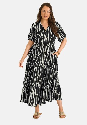 Frau trägt ein schwarz-weißes Midi-Kleid mit Zebramuster, Knopfleiste, kurzen Puffärmeln und beigen Sandalen mit offenen Zehen.