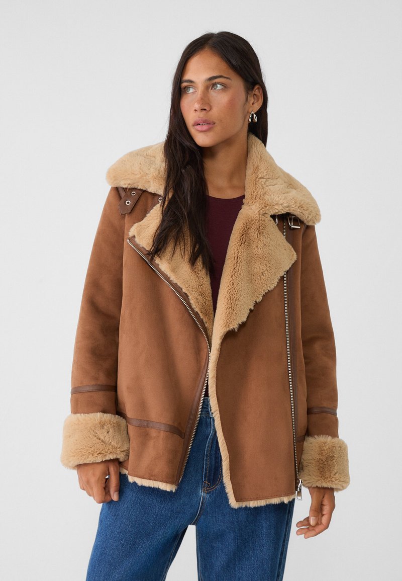 Braune Kunstschafsfutterjacke mit breitem Kragen, Reißverschluss und hellbraunen Akzenten; verfügt über eine weiche Textur und plüschige Bündchen.