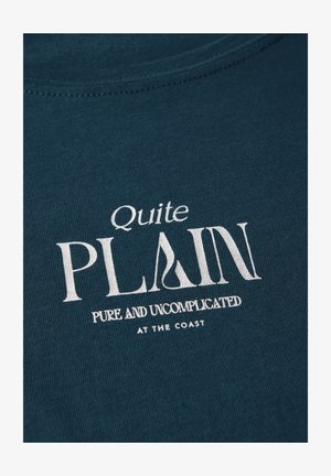 T-shirt teal à manches courtes en tissu côtelé, arborant un texte blanc disant "Tout à fait PLAIN" et "PUR ET SANS COMPLICATION À LA CÔTE".