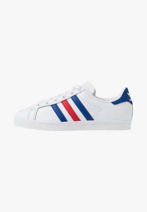 Zapatilla baja blanca de Adidas con rayas azules y rojas, cordones blancos y lengüeta azul en el talón con el logo de Adidas.