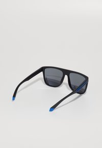 Ochelari de soare negri cu lentile gri, formă rectangulară, cadru mat texturat și accente albastre pe brațe.