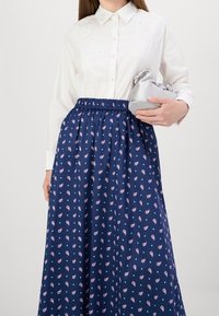 Valkoiset kauluspaita, jossa on brodeerattuja yksityiskohtia, yhdistettynä pitkä, tummansininen hame, jossa on kukkakuosi ja joustava vyötärö, pitäen hopeista clutch-laukkua.