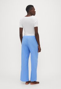 Wit kort mouwtopje en lichtblauwe wijde broek. De broek heeft een elastische tailleband met merkinformatie. Eenvoudig ontwerp, gladde textuur.