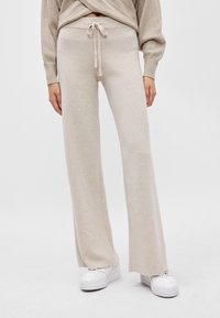 Beige παντελόνια με φαρδιά πόδια κ αι κορδόνι στη μέση, φτιαγμένα από μαλακό ύφασμα, με λεία υφή και άνετη εφαρμογή. Συνδυασμένα με λευκά αθλητικά παπούτσια.