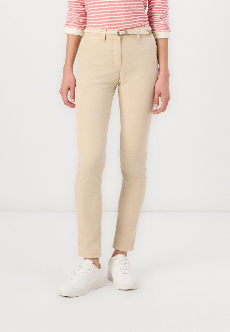 Pantaloni beige slim-fit realizzati in cotone, con un design classico, vita intermedia e una leggera texture. Abbinati a sneaker bianche.