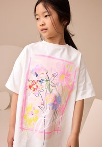 T-shirt en coton blanc avec un imprimé floral coloré comprenant des fleurs roses, jaunes et bleues à l'avant. Coupe décontractée et manches courtes.