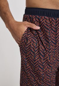 Geprinte broek met een marineblauwe tailleband, voorzien van een herringbonepatroon in rood, oranje en crème kleuren. Inclusief zijzakken.