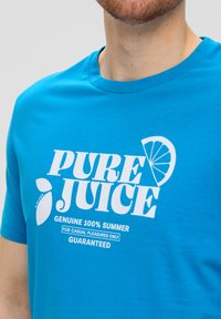 Blauwe katoenen t-shirt met witte bedrukte tekst "PURE JUICE" en een citroentekening. Korte mouwen en een klassieke ronde hals.