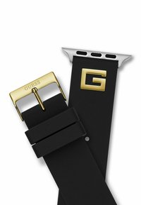 La correa de reloj de caucho negra cuenta con una hebilla de metal en tono dorado grabada con "GUESS" y un accesorio en tono plateado con un acento dorado en forma de "G".