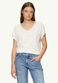 Witte V-hals t-shirt met opgerolde korte mouwen, gemaakt van zachte katoen. Gecombineerd met lichtblauwe versleten jeans, die een relaxed fit laten zien.