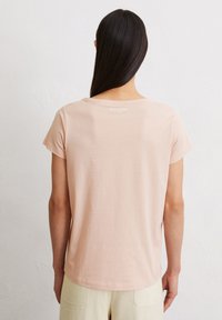 Lichtroze t-shirt met korte mouwen, gemaakt van zacht materiaal, ronde halslijn, met een klein logo op de bovenrug, gladde textuur.