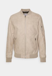 Chaqueta bomber beige hecha de suave material de ante, con cierre delantero, puños acanalados y un bolsillo con cremallera en el brazo izquierdo. Textura suave.