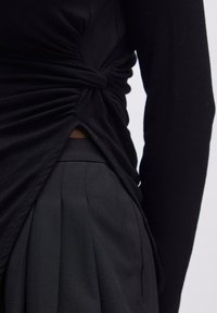 Schwarzes Langarmtop mit gerippter Textur und gedrehtem Design an der Taille, kombiniert mit hoch sitzenden schwarzen, plissierten Hosen.