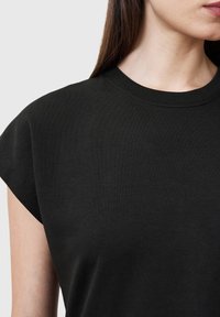Camiseta negra de manga corta hecha de algodón suave. Presenta un cuello redondo y mangas ligeramente alargadas. Textura lisa.