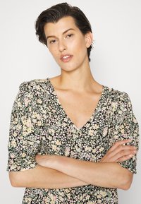 Vestido floral com fundo preto, decote em V, mangas puff curtas e pequenos padrões de flores em tons pastéis. Tecido suave com uma leve textura.