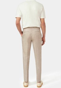 Pantaloni in lino beige chiaro con vestibilità dritta, due tasche posteriori e una texture sottile. Abbinati a una camicia bianca a maniche corte e scarpe.
