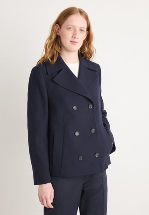 Merino peacoat valmistettu villasekoitteesta, jossa on kaksinkertainen nappikiinnitys, suuret mustat napit ja sivutaskut. Sileä pinta.