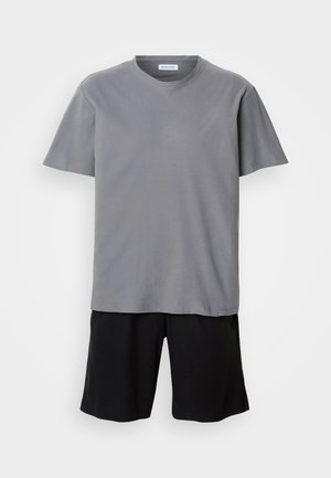 T-shirt gris à manches courtes et col rond, associé à un short noir atteignant les genoux, sur fond blanc uni.