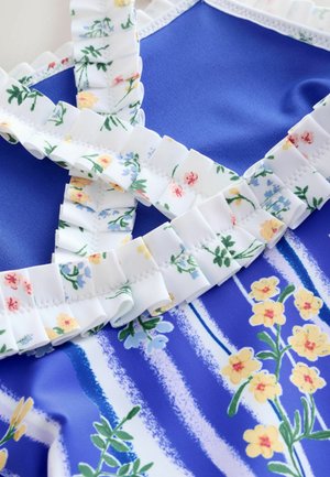 Badetøj med blåt, glat stof med hvide blomsterflæser, dekoreret med gule, pink og blå blomster på en stribet baggrund.