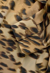Blouse à imprimé léopard en beige et marron, en tissu lisse, dotée d'un poignet boutonné avec un bouton marron et de détails cousus.