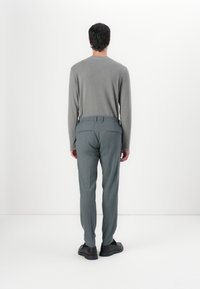 Lange mouwen lichtgrijs shirt gecombineerd met textuur, op maat gemaakte lichtblauwe broek en zwarte schoenen, gezien vanaf de achterkant. Eenvoudige achtergrond.