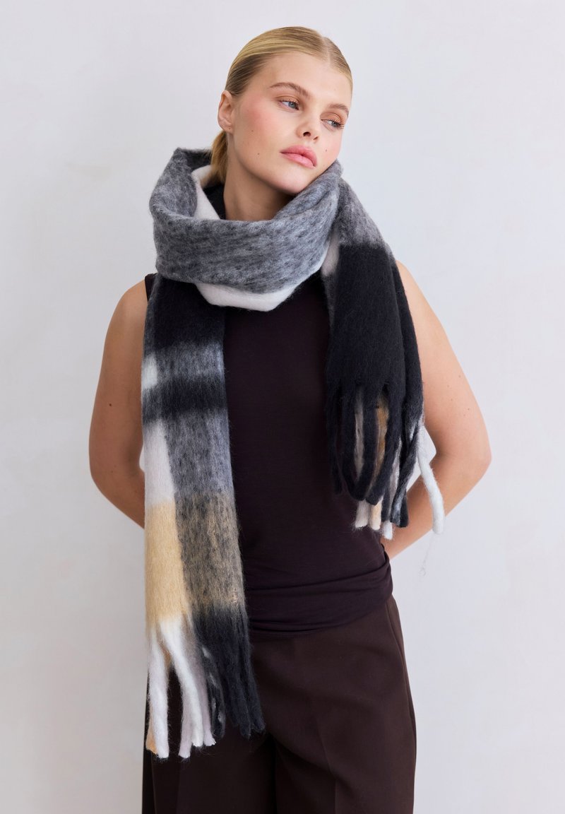 Écharpe en laine présentant des nuances de noir, gris et crème avec des extrémités à franges, affichant un motif de dégradé subtil et une texture douce.