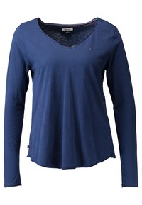 Pitkähihaisen, tummansinisen paidan V-pääntiellä, joka on valmistettu pehmeästä kankaasta; siinä on pyöristetty helma ja pieni logo rinnassa.