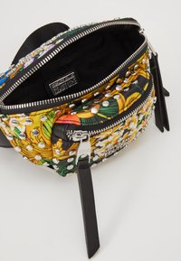 Torba z materiału w kwiatowy wzór, ozdobiona srebrnymi ćwiekami, z zamkiem błyskawicznym i czarnymi akcentami. Kompaktowy design z widoczną etykietą wewnętrzną.