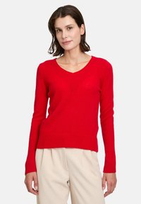 Pull rouge à col en V fabriqué en maille douce, avec des manches longues et un ourlet côtelé. Conçu pour un silhouette ajustée.