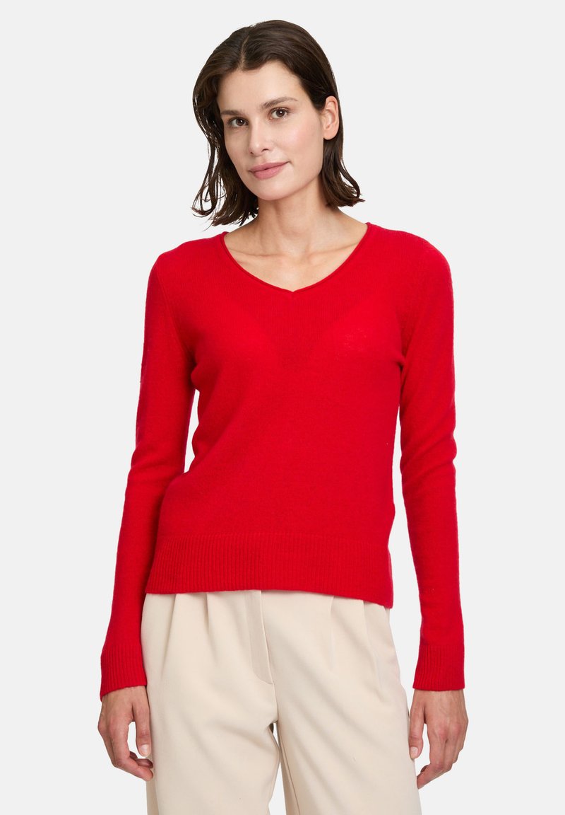 Pull rouge à col en V fabriqué en maille douce, avec des manches longues et un ourlet côtelé. Conçu pour un silhouette ajustée.