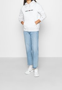 Lichtgrijze hoodie met trekkoord, met het "TOMMY JEANS" logo. Gecombineerd met lichtblauwe straight-leg jeans en witte sneakers. Eenvoudige, casual stijl.