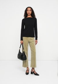 Zwarte lange mouwen top, lichtgroene corduroy broek, zwarte handtas met hardware accenten, en zwarte puntige hakken met blokhakken.