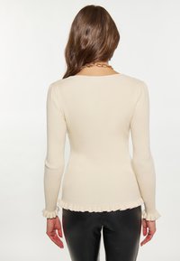 Pulover cream, cu model la baza, cu mâneci lungi, având manșete și tiv frațate. Materialul pare moale și ușor texturat.