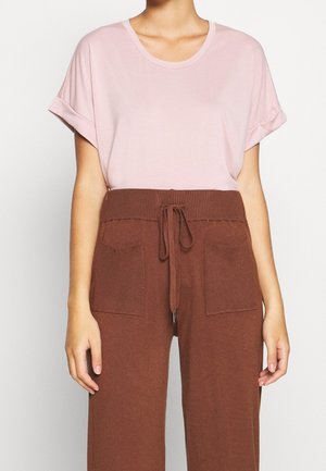 T-shirt rose clair à manches courtes avec un col rond, associé à un pantalon marron taille haute avec une ceinture côtelée et deux poches avant.
