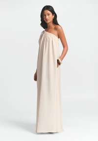 Rihmata ilma õlakuvari beez maksikleit, kogutud kaeluse ja voolava kangaga, küljetaskutega. Materjal näeb välja kerge ja sile tekstuuriga.