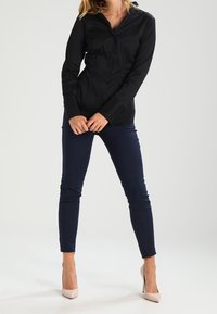 Chemise noire à boutons avec un col, associée à un pantalon ajusté bleu marine et des talons roses pâles. Textures lisses, coupe ajustée.